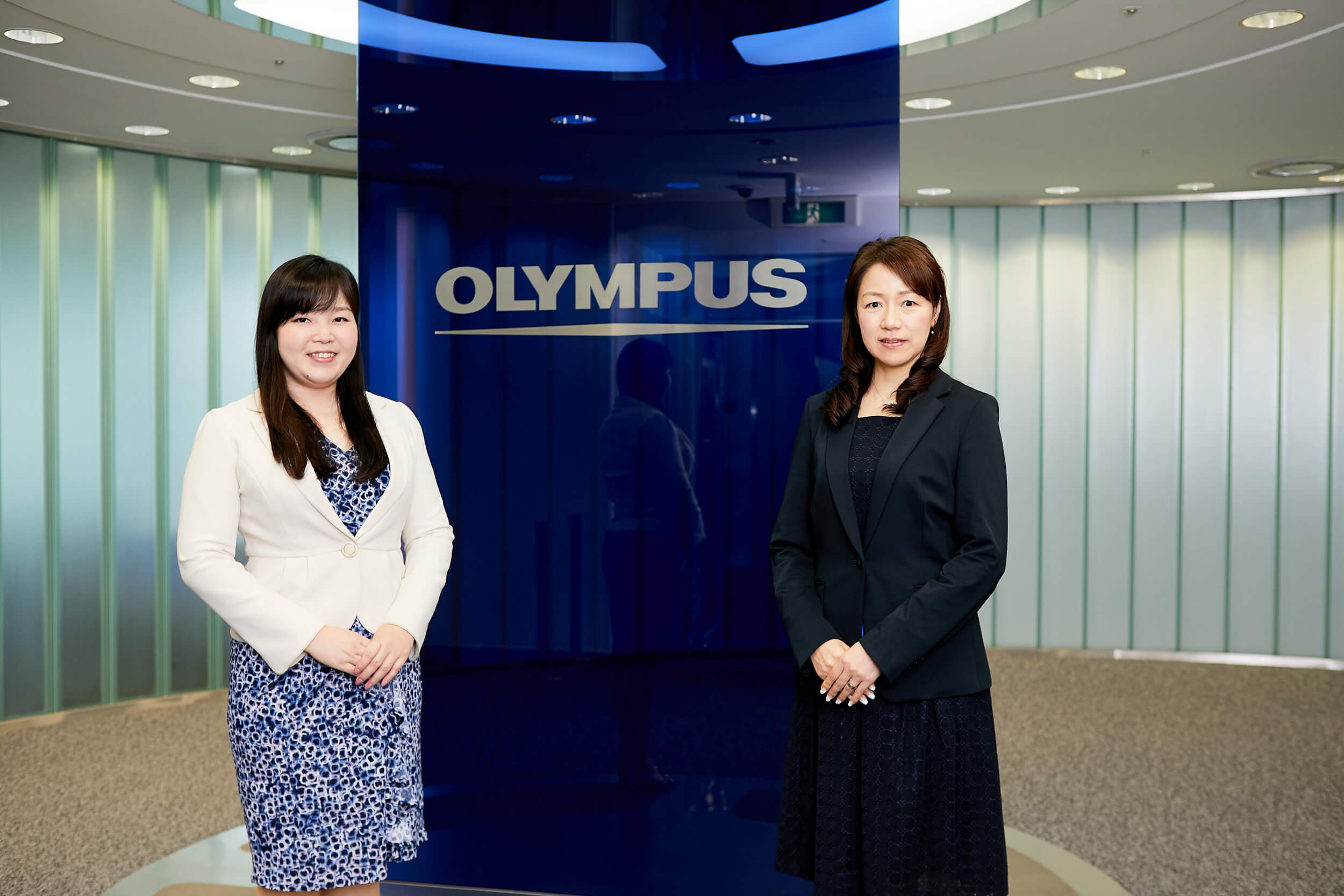 OLYMPUSのロゴを背景にしたオリンパスのお客様2名